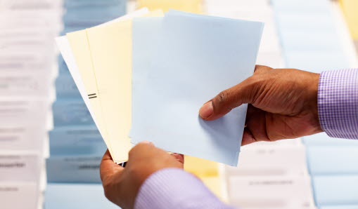 Händer som håller i valkuverten framför en monter med valsedlar.