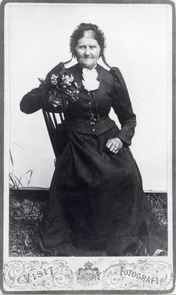 Kristina Andersson från Kårsta levde 1823-1908. På bilden är hon 85 år. Fotograferat utomhus, se den ljusa fonden och gräset, kanske på någon marknad. Kristina var mormors mors till Margit Svärd på Sunnarby gård i Kårsta