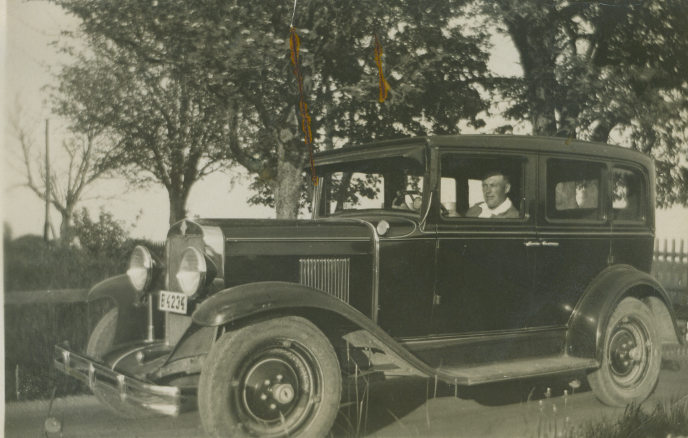 I bilen sitter John Johansson. Paret Sally och John Johansson ägde Vada affär och John drev även taxirörelse och skolskjuts. Affären stängde 1961. Sally och John var de första i bygden som hade tv.