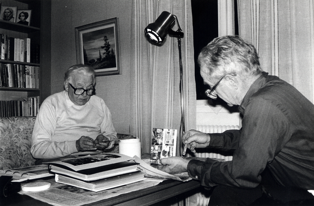 Studiecirkeln Ejnar Carlsson - en man och hans bilder arbetar hemma hos Sven Billersjö på Billsta gård i Frösunda. Bonden Ejnar Carlsson, arrenderade tillsammans med sin bror Emil Frösunda prästgård, testamenterade sina fotografier till Frösunda hembygdsförening. I samarbete med Studieförbundet Vuxenskolan har man arbetat med att ordna fotosamlingen. Vid bordet sitter t v Sigvard Jansson  och Sven Billersjö sysselsatta med att ta bord de tejpbitar som fotografierna är fastsatta i albumen med. I stället fästs korten med arkivvänligt lim