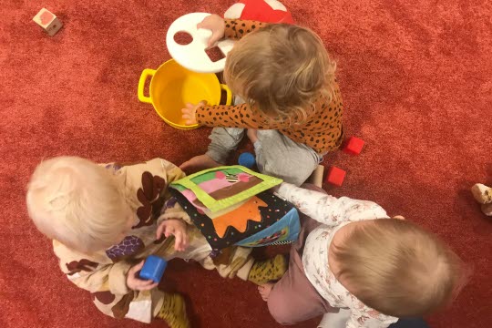 Tre bebisar som sitter på golvet och leker med leksaker