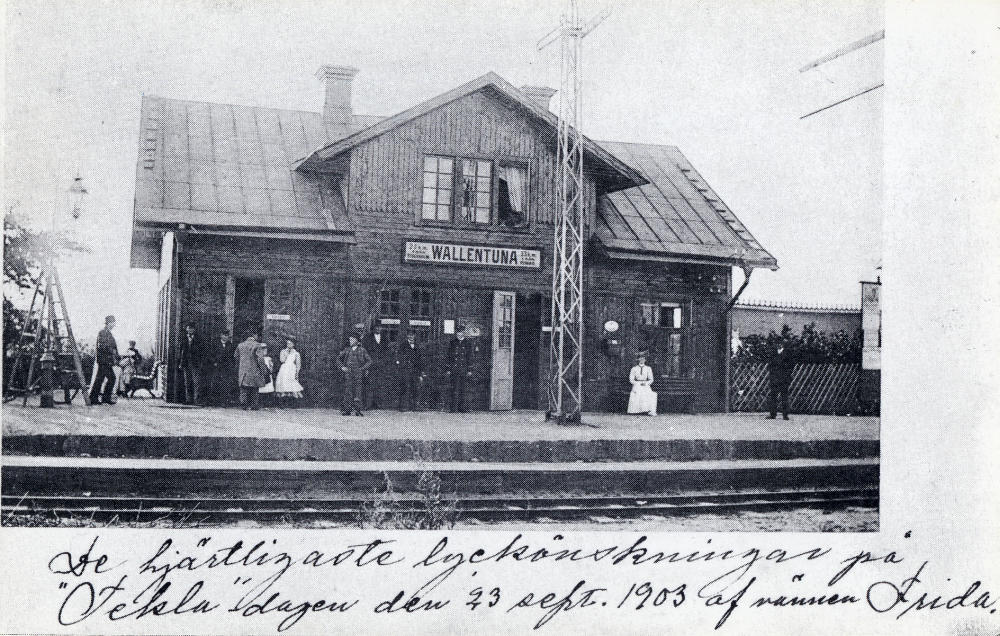 Framför Vallentuna järnvägsstation står stationspersonalen och flera andra personer. Framför stationshuset står en semafor.
