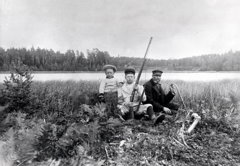 Den siste dragonen i Vallentuna, Johan August Rönn sitter vid Ubbysjön, Pyttsjön, tillsammans med sonen Ruben Rönn med ett gevär i handen och dottersonen Ragnar Jansson. På andra sidan sjön syns hus i Gröndal vid Lingsbergsvägen