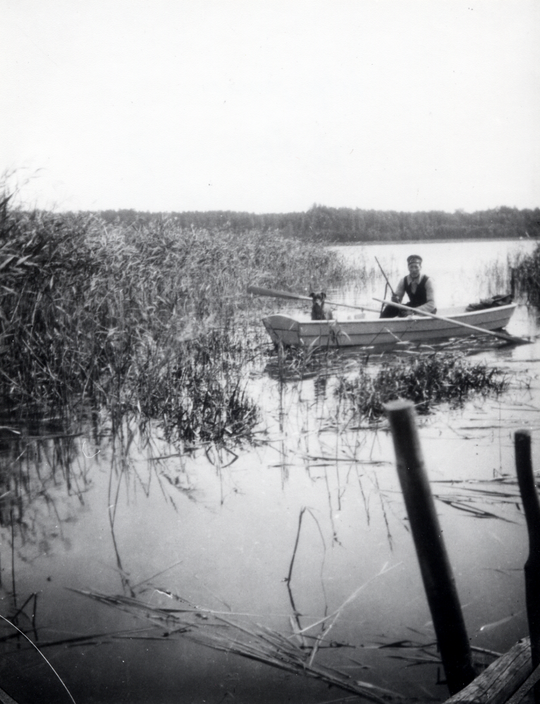 Helge Jansson i en roddbåt tillsammans med hunden Ketty  i vassen i Vallentunasjön.