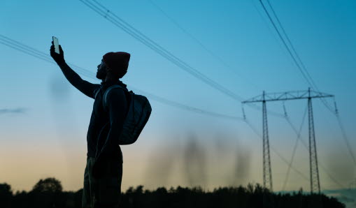 Siluetten av en man som håller upp en mobiltelefon mot himlen.