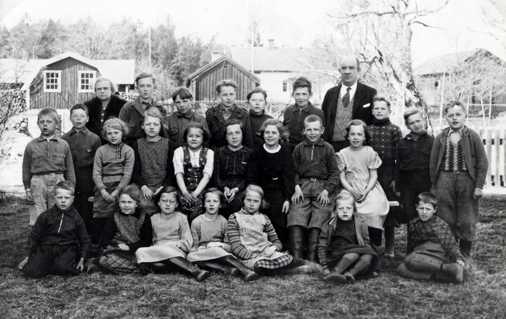 Vada skola.  I bakgrunden syns Vadaby. Bakre raden fr v lärarinnan Olga Pettersson, klasserna 1 och 2, Edgar Axzell Seneby, Gunnar Gustavsson Seneby, Bernt Svanström Vadaby, Åke Ek Målsta, Henry Bjurström Lilla Benhamra, Brynolf Fromm lärare i klasserna 3, 4, 5 och 6, Bengt Wester Lussinge, Arne Bjurström Lilla Benhamra och Harry Frölin Vadatorp. Rad 2 sittande fr v Bertil Mattsson Brotorp, Gösta Karlsson Rosendal, Gerd Enroth Seneby, Märta Mattsson Brotorp, Anna-Greta Gustavsson Seneby, Axelin Andersson, Barbro Enroth Seneby, Nils-Erik Eriksson Lugnet och Anna-Lisa Eriksson Lugnet. Rad 3 sittande på marken Gunnar Ahlén Lilla Benhamra, Axelina Andersson Målsta, Ruth Jonsson Kråktorp, Märta Jonsson Kråktorp, Irene Eriksson, Astviol Mattsson Brottby och Karl-Uno Mattsson Seneby.  Uppgifter från Bengt Wester, Lussinge gård, Brottby