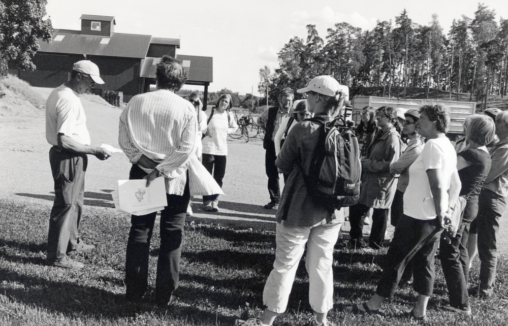 Personalen vid Vallentuna bibliotek samlas vid Mellangården i Kragsta för att cykla till Eva Rahmqvists sommarstuga Lillsätra vid Vallentunasjöns strand nedanför Oppgården.  Ove Rick, t v, berättar och visar en modern gård.  Ove, hustrun Madeleine, sonen Anders och hans fru Heléne driver Mellangården och Lövhagen med bl a mjölkkor. Runt honom står bl a fr v Eva Rahmqvist, Lena Drevemo, Inga-Lena Boström, Hase Danielsson, Anna-Karin Wikman, Anna Bergström, Susanne Engström, Eva-Lena Granbacka, skymd, Charlotta Mickelsson, Anita Hofving, Kerstin Berglund, Pirkko Mickelsson, skymd och Anna Brynell.