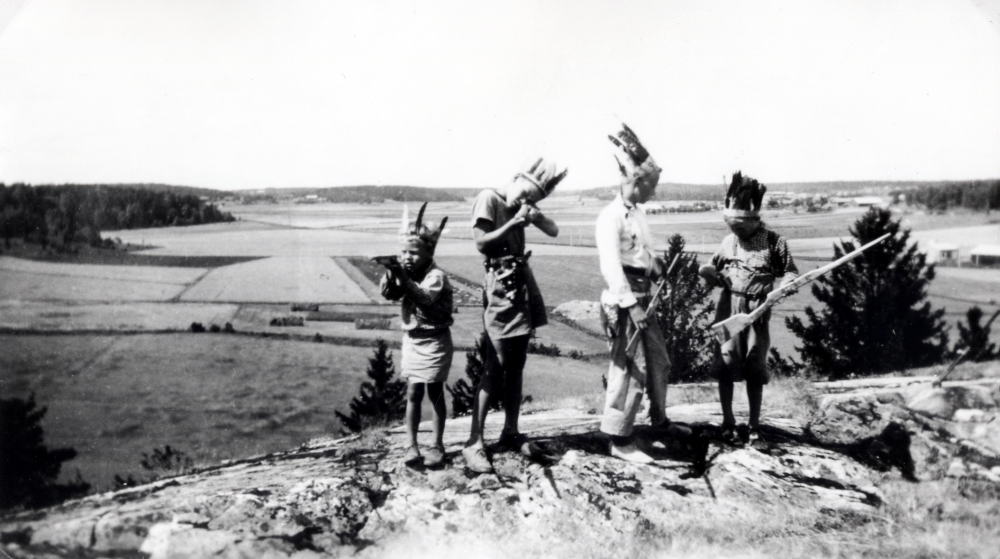 Lek på berget utanför magasinet vid Ekskogens gård.  I bakgrundens t h syns Ekskogens träförädling och i bildens mitt Salby gård.  Pojkarna är fr v Karl-Erik Nyberg, Sami Suomalainen, Timos bror, Timo Ekholm och Birger Nyberg.  

Timo och hans lillebror Sami kom till Sverige som finska krigsbarn 1944. Timo adopterades senare av ägarparet på Ekskogens gård i Kårsta, Inez och Manfred Ekholm. Läs mer i Timo Ekholms bok Krigsbarn 40.
