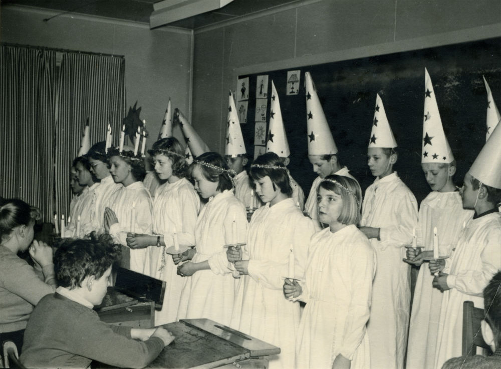 Luciafirande i Vada skola;  Luciafirande i Vada skola.  Pojken i bänken t h är Arne Andersson.  I luciatåget står tärnorna i främre ledet fr v Agneta Jansson,Birgitta Johansson, Lucia Elisabeth Ericsson, Britt-Marie Mattsson, Eva Alstermark, Anita Andersson och Siv ?.  Pojkarna fr h Jan Erik Johansson, Stig Erik Karlsson, Bo Grönborg, Björn Westberg övriga okända