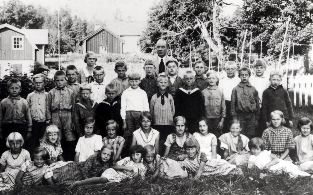 Lärarna Olga Pettersson och Brynolf Fromm tillsammans med eleverna på skolgården utanför Vada skola.  Stående fr v står Hans ?, Seved Eriksson, David Thun, Karl-Erik Thun, okänd, Sture Karlsson, okänd, Harry Thun, Sven-Erik Johansson, Hans Andersson, Karl Åkerblom, Bernt Karlsson, Åke Karlsson, Ruben Karlsson,  Stig Andersson, Nils Sjöberg, okänd, okänd och Rejne Burström.  Sittande fr v Anna-Lisa Ahlén, okänd, Harriet Burström, Ingegerd Singfeldt, Ella Eriksson, Maj Hoffman, Gunvor Andersson, Vivvi Wahlin, Märta Eriksson och Maj-Lis Johansson.  Liggande fr v Maj-Britt Johansson, Axelina Andersson, Märta Karlsson, Ingrid Wester, Ulla Eklund och Barbro Eneroth
