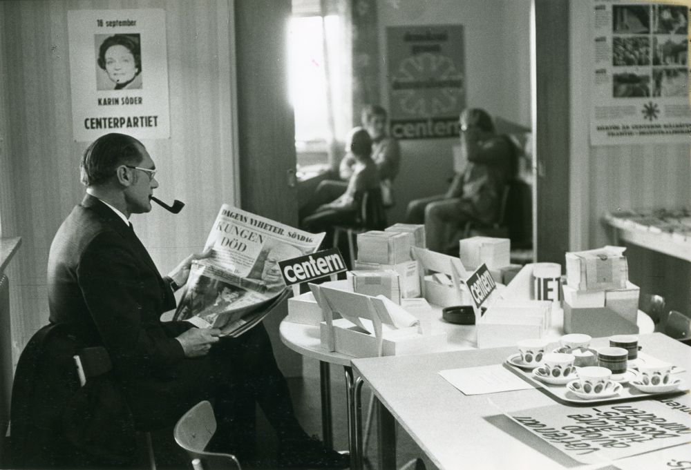 Interiör från Centerpartiets valbyrå på Allévägen. Carl-Erik Wikström läser Dagens Nyheter på valdagens morgon klockan 07. Tidningens förstasida domineras av nyheten om kung Gustaf VI Adolfs död under gårdagen den 15 september 1973.
•Fotografiet ingår i bildserien ”Vardagsliv i Vallentuna kommun” av Rachael Gough-Azmier & Gunilla Blomé, Haga Studios HB.