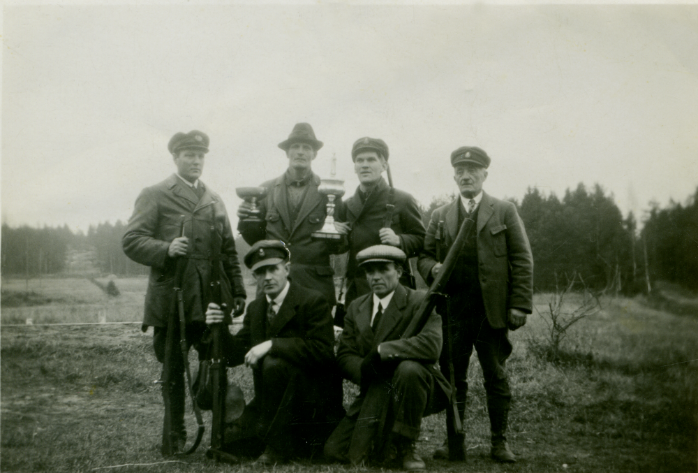 "Mästerskyttar?" är textat bredvid fotot. Skyttarna står med sina gevär och två pokaler. I bakre raden står längst till höger 
 Ferdinand Lindström född 1871 och tvåa från vänster står Emanuel Bornholm född 1909. Övriga okända men troligen är alla medlemmar i Vallentuna skytteförening där Ferdinand Lindström var med. Årtal saknas.