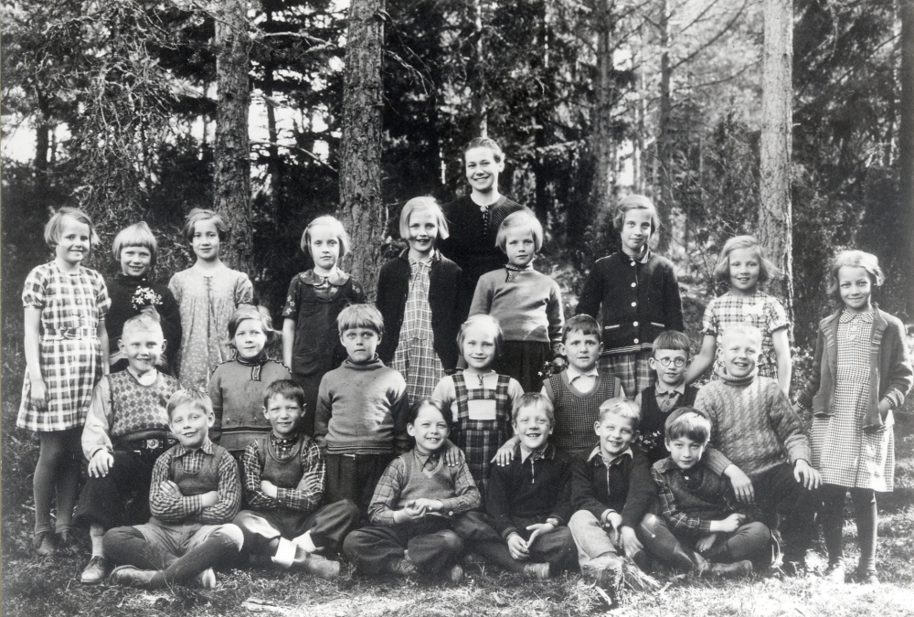Lärarinnan Margit Löfgren, senare gift Hovne, tillsammans med skolbarnen i Hjälmsta skola. Övre raden fr v Ann Marie Hagman, Gudrun Frölin, ? Molin, Greta Noaksson, Elsy Hedlund, Ulla Karlsson, Anna-Greta Nordgren, Marianne Johansson, och Eihild Wallin. Mittenraden fr v Ragnar Nordström, Maj-Britt Frölin, okänd, Solveig Sjögren, Karl Arne Hedlund, Hans Lindström och Göran Adolfsson. Nedre raden fr v Herbert Johansson, Rune Holmberg, Lennart Hovmark, Berndt Noaksson, Lars Larsson och Lennart Holmqvist