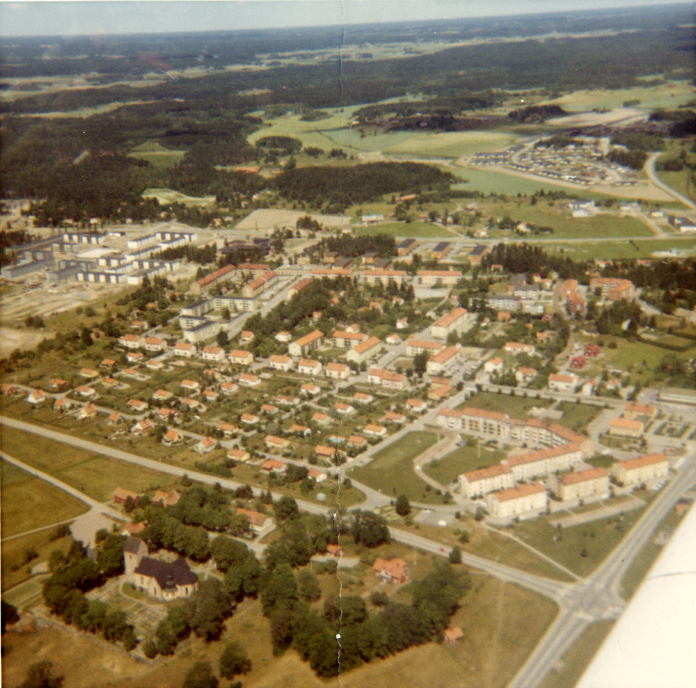 Flygbild över Vallentuna centrala delar. I förgrunden Vallentuna kyrka, i mitten Prästgårdsgärdet, Centralvägen, Allévägen och Rickebyhöjd. Längst upp t v byggs bostadsrättsföreningen Norrgården. Sörgården har ännu inte påbörjats. Längst upp th enfamiljshus i Snapptuna