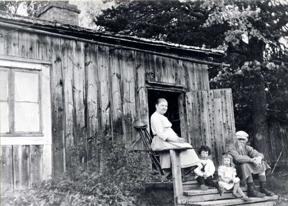 Ljungbacken i Löfsta. På trappan sitter Berlin, korgmakare och fiskare. Han var så gott som blind. Berlin hade varit kusk på Löfsta. Hans hustru Hanna Berlin sitter på trappräcket. De små barnen är sommarbarn från Stockholm. Frösundaborna har inte hört talas om att Berlin var blind eller att han var korgmakare
