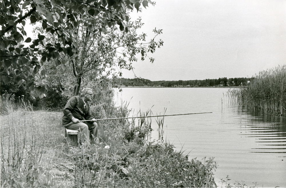 Folke Almgren sitter och metar nedanför Vallentunatvätten, tvätteriet vid Vallentunasjön.  
•Fotografiet ingår i bildserien ”Vardagsliv i Vallentuna kommun” av Rachael Gough-Azmier & Gunilla Blomé, Haga Studios HB.