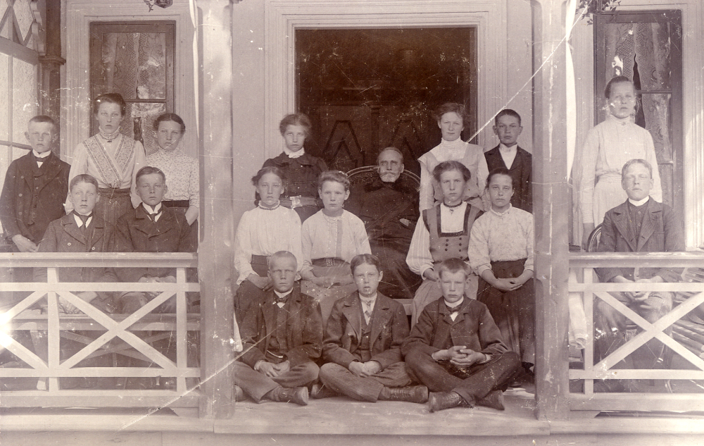 Össeby-Garns prästgård. Mitt på verandan sitter kyrkoherde Karl Hedén om given av barn och ungdomar. Karl Oskar Hedén var kyrkoherde i Össeby-Garns församling 1883-1914. Uppgift om fotoår saknas.