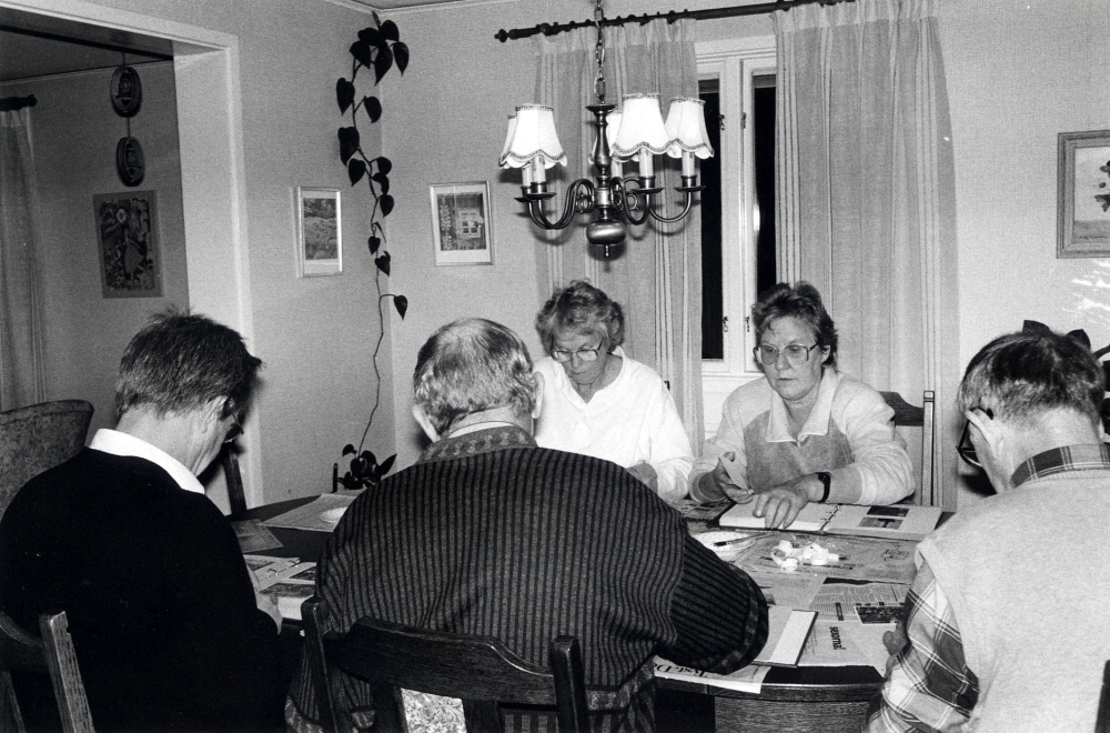 Studiecirkeln Ejnar Carlsson - en man och hans bilder arbetar hemma hos Sven Billersjö på Billsta gård i Frösunda. Bonden Ejnar Carlsson, arrenderade tillsammans med sin bror Emil Frösunda prästgård, testamenterade sina fotografier till Frösunda hembygdsförening. I samarbete med Studieförbundet Vuxenskolan har man arbetat med att ordna fotosamlingen. Vid bordet sitter  med ryggen mot kameran fr v Olle Wredh, Harry Öhrlund och Stig Öhman.  På andra sidan fr v Ulla Öhrlund och Kerstin Mannerfelt.  Alla deltagare petar bort den kladdiga tejp som bilderna är fästa med i albumen.  I stället använder man arkvibeständigt lim