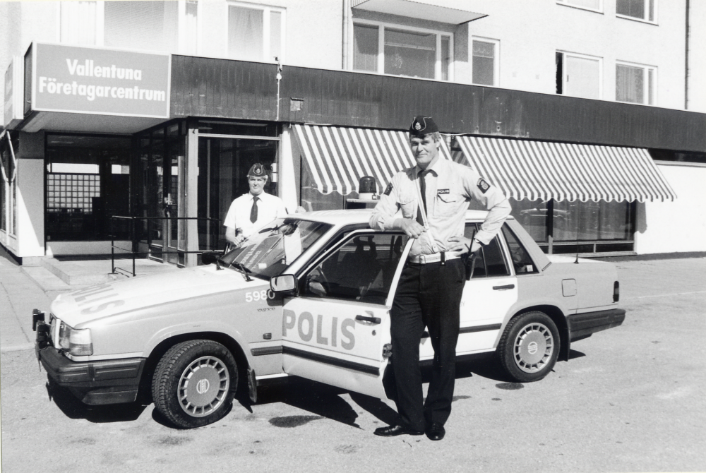 Polisbil utanför Vallentuna företagarcentrum.  På bilens vänstra sida står inspektör Eva Braghe och t h polisassistent Roger Pettersson