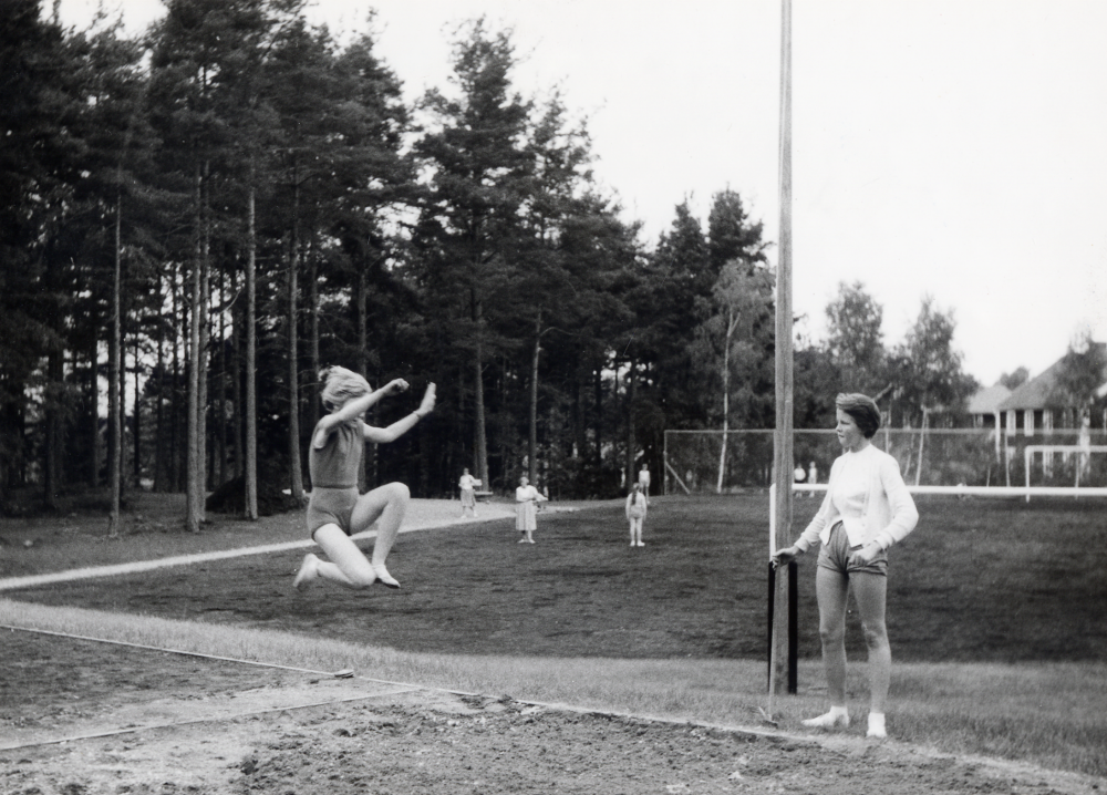 Invigning av skolidrottsplatsen vid Hjälmsta skola. Gunborg Karlsson gör invigningshoppet i längdhopp. I bakgrunden syns Gamla ålderdomshemmet