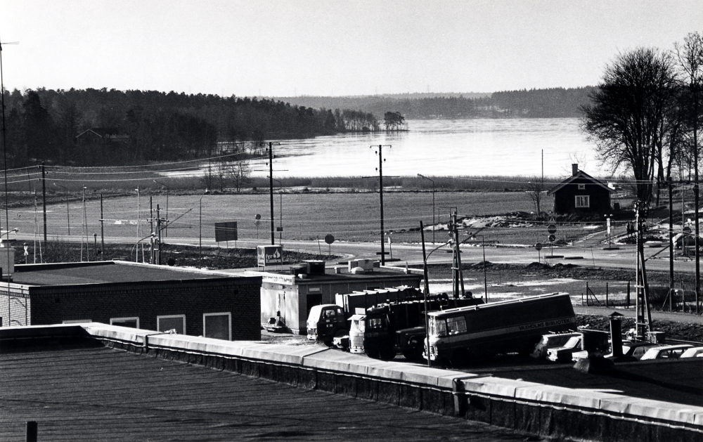 Utsikt över Vallentunasjön från Tellus-Maskin. I förgrunden Industrivägen med Elverket, Grillkiosken och parkerade bilar och buss. T h syns tvättstugan som hör till Vallentuna prästgård