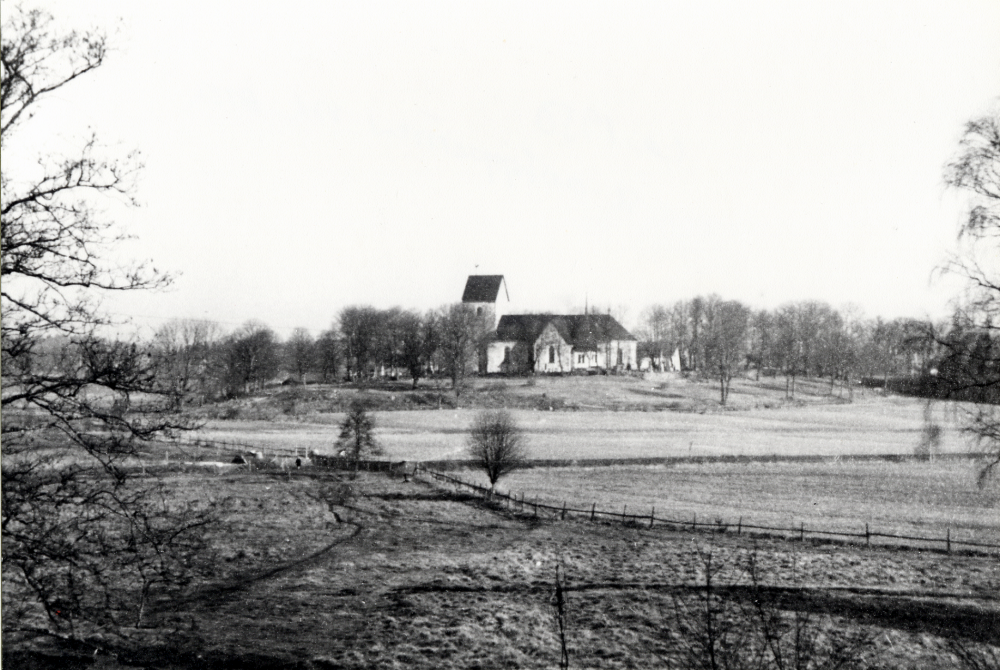 Utsikt från Högbo i Bällsta mot Vallentuna kyrka.  Observera avloppsrör vid Ormstaåns utlopp.  Marken närmast Vallentunasjön, som ligger t v i bilden, är täckt med tuvgräs. Inhägnad är kyrkans jordbruksmark