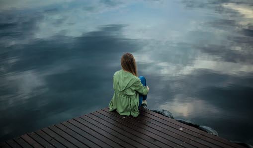 Ung kvinna sitter på brygga vid vattnet