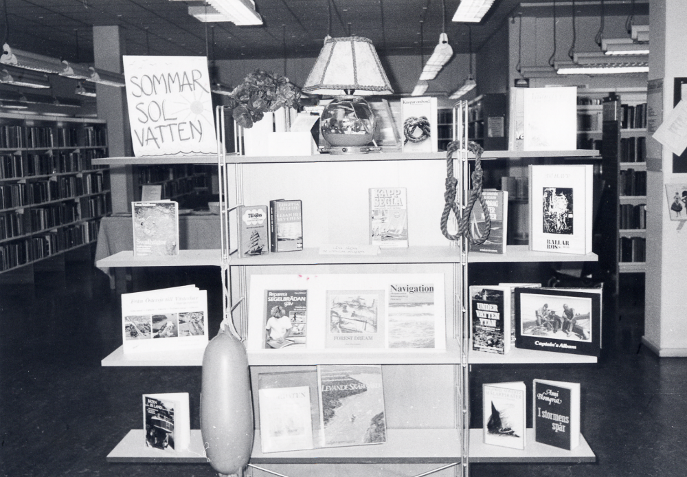 Miniutställning i Vallentuna bibliotek med tema Sommar - sol - vatten sammanställd av Gunvor Svensson. På en hylla vid katalogskåpet gör personalen små miniutställningar som varar ca 1 månad