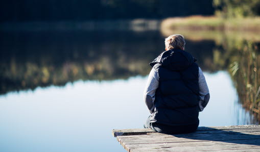 Person sitter vid brygga och tittar ut på vattnet.