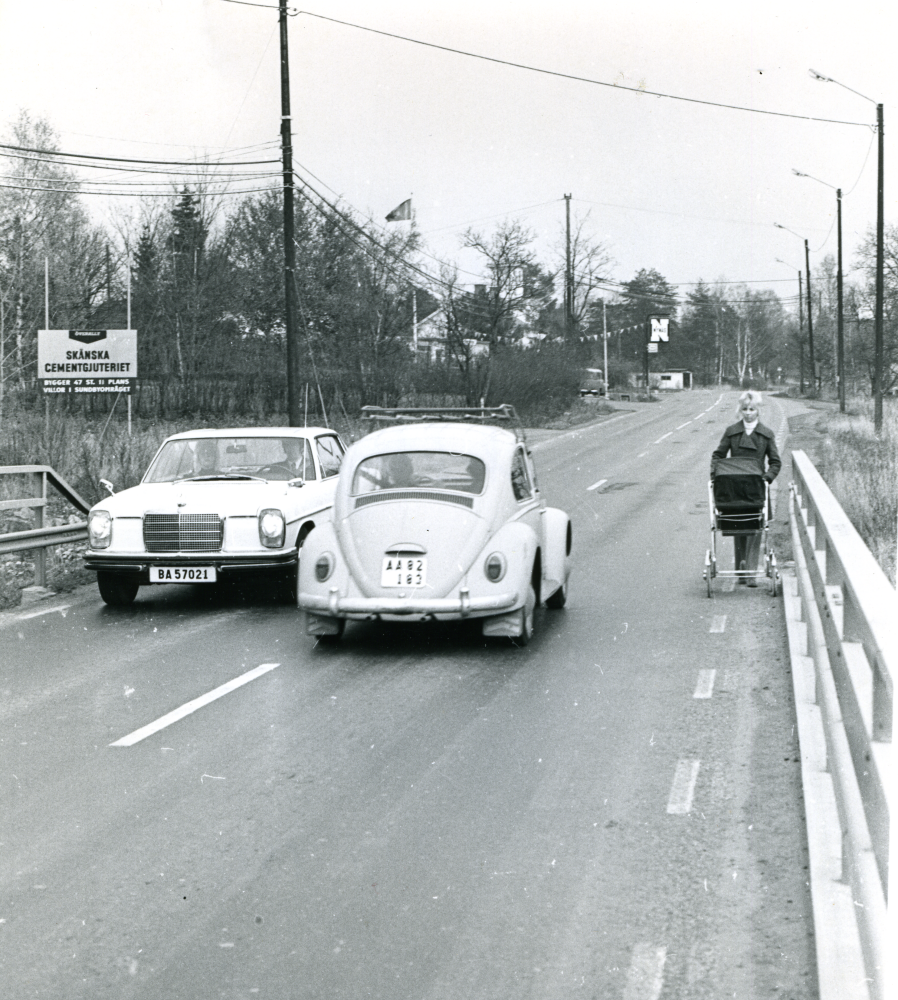 Bro över Husaån;  Trafikträngsel på bron kan vara ett bildmässigt argument för att anordna den gång- och cykelbro som byggdes efter att fotot togs. Bron placerades ungefär där reklamskylten står uppställd. 