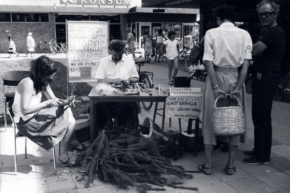 Vallentuna folkdansförening visar olika aktiviteter på Tuna torg. Eva Rahmqvist gör grötkräklor av tall, Erland Rost täljer i trä. Hannah Schuldt och Ingmar Unnerstad tittar på.