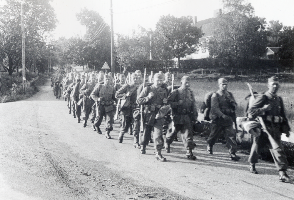 Rimbo skolkompani utrustas vid landstormsförrådet nr 46d vid mobiliseringen 1939. Här marscherar mannarna ner längs Skolvägen förbi Vita skolan i Hjälmsta