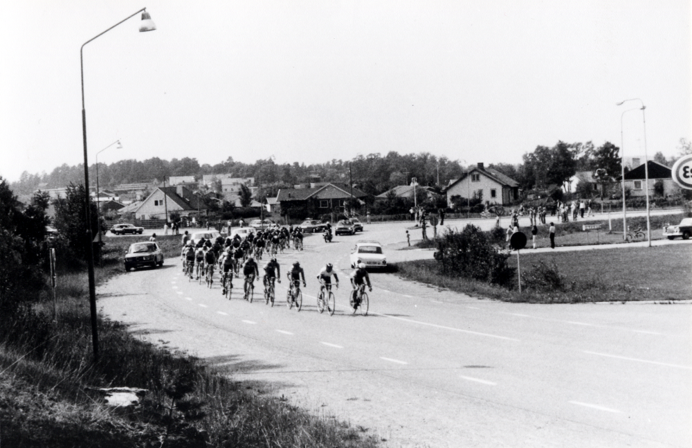 Cykeltävlingen 'sex-dagars' passerar Vallentuna 1973. Här har en klunga cyklister svängt in från Stockholmsvägen på Karlsbergsvägen vid Esso bensinstation