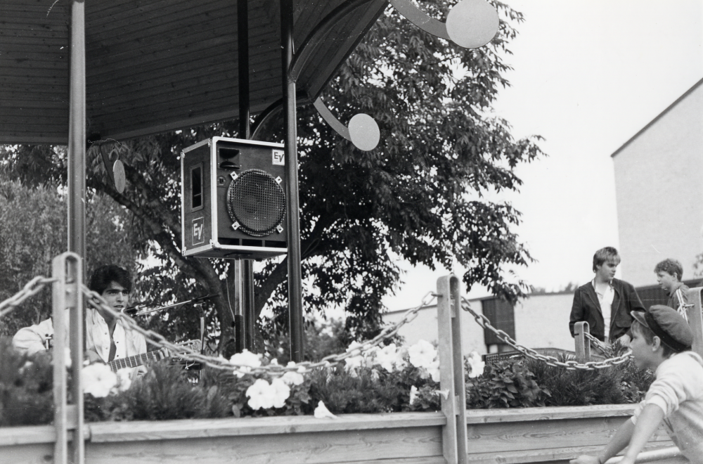 Milton Cortez spelar gitarr i Musik på torget sommaren 1985 i paviljongen på Tuna torg.  Pojken i mörk jacka är Tomas Larsson, ljudtekniker?