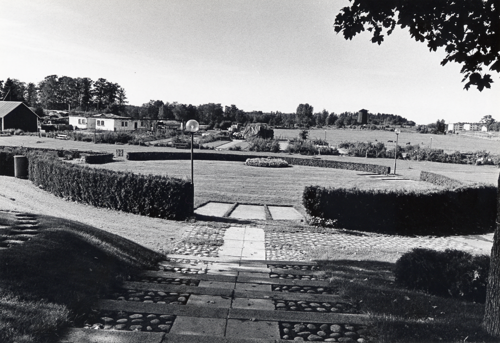 Vallentuna kyrkogård har byggt ut med bl a en minneslund. T v syns ladugården till Vallentuna prästgård, nedbrunnen, endst muren finns kvar. T h skymtar bostadsområdet Sörgården samt i bildens mitt Väsby kvarn