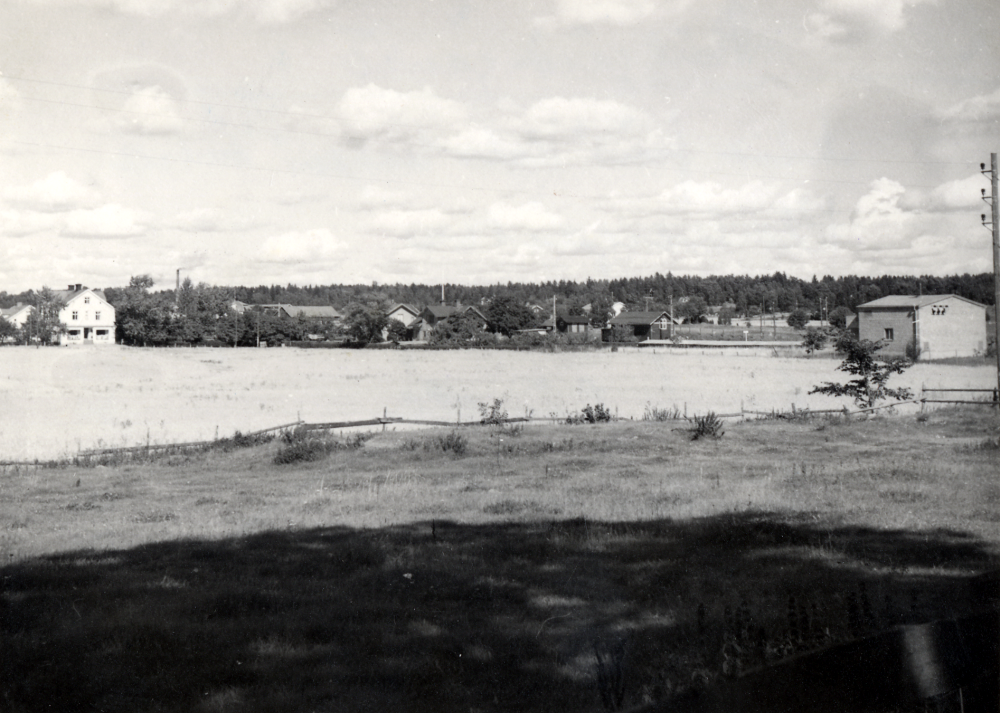 Utstiktsbild över det obebyggda Prästgårdsgärdet i Vallentuna. T v Tibells affär, Vallentuna tegelbruk och Vallentuna järnvägsstation och Vallentuna järnvägshotell Flugan. Längst t h en transformatorstation som tillhör järnvägen. Bilden har fotograferats från den s k Kalvhagen öster om Klockargården.