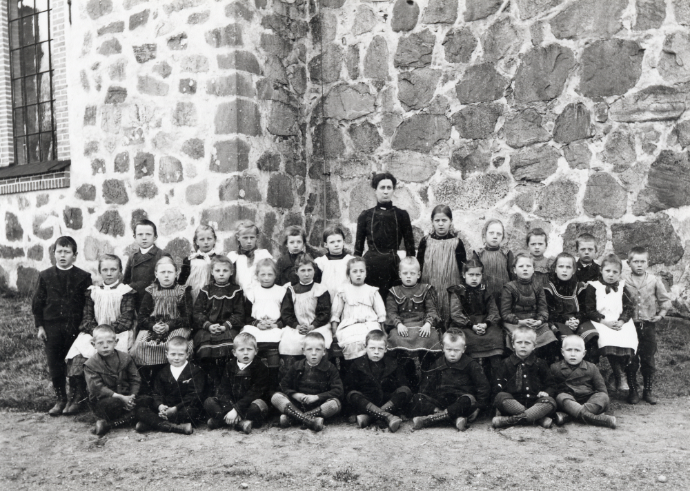 Lärarinnan Anna Gauffin fotograferad tillsammans med skolbarnen utanför  Vallentuna kyrka.  I bakre raden nr 3 fr v är Hildegard Olsson Åby gård