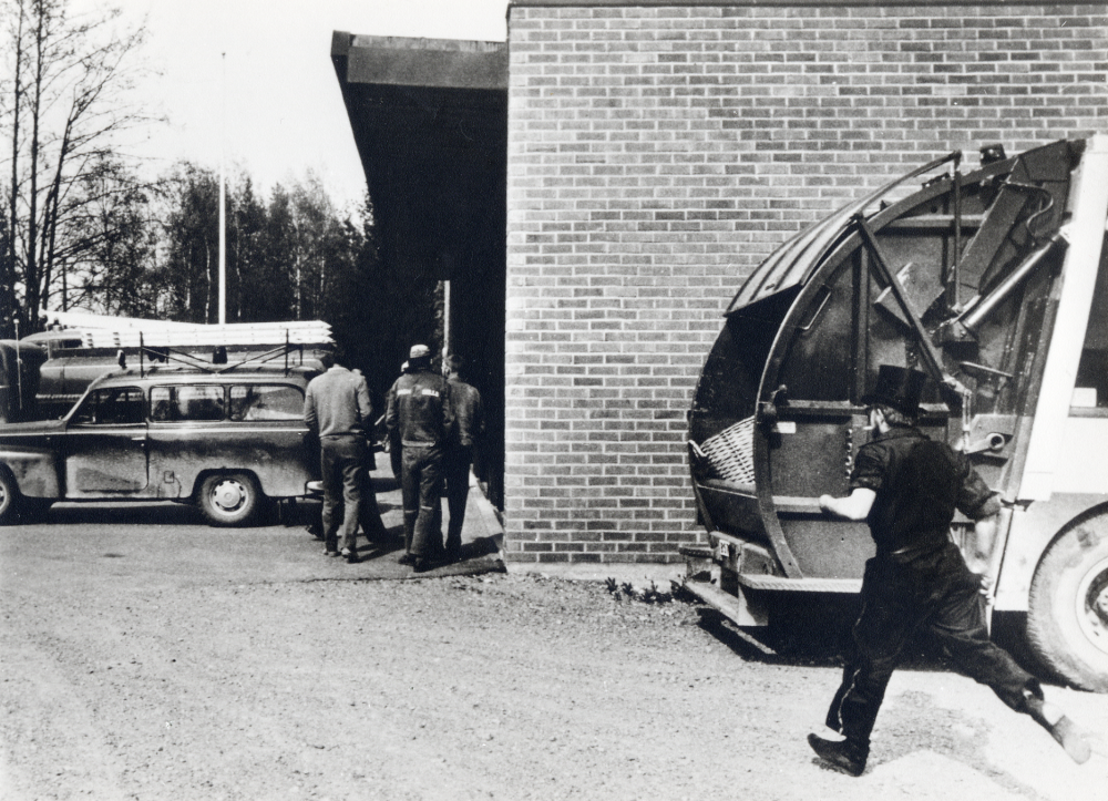 Brandlarmet har just gått och borgarbrandkåren samlas vid brandstationen för utryckning. T h kommer sotare Sven-Olof (Henrik) Henriksson springande. Henrik var sotare i Vallentuna från mitten av 1960- till mitten av 1990-talet.