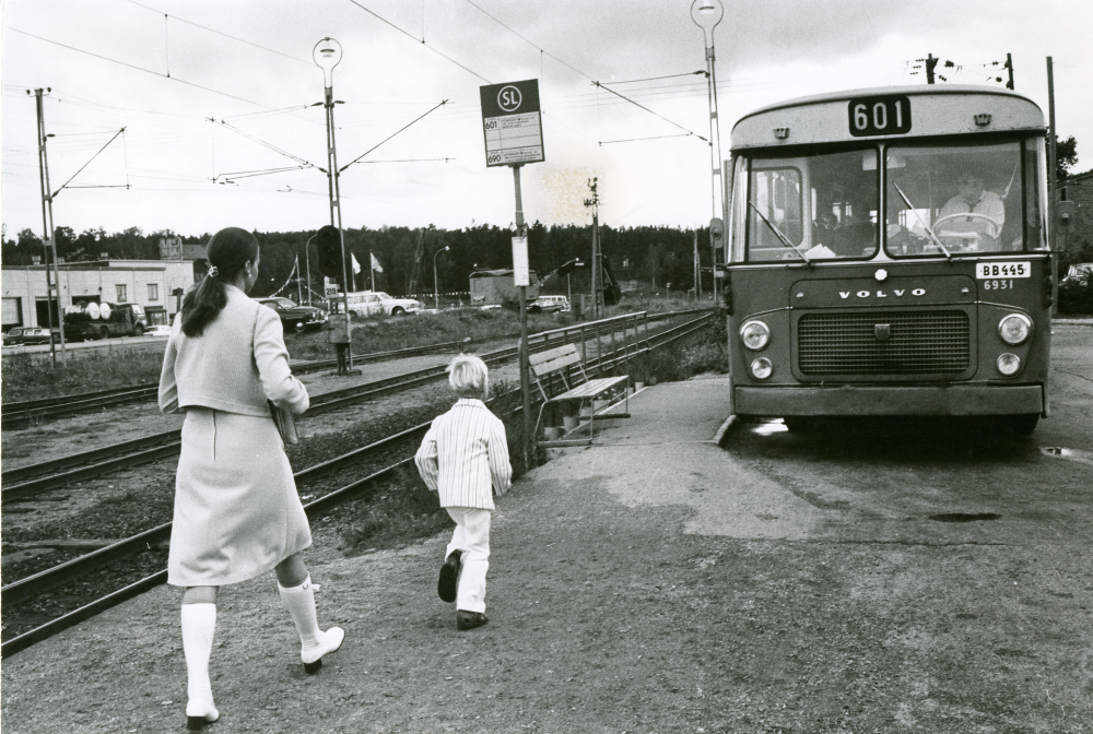 Resenärer på väg till buss 601 som stannat till  på busshållplatsen vid stationen.

•Fotografiet ingår i bildserien ”Vardagsliv i Vallentuna kommun” av Rachael Gough-Azmier & Gunilla Blomé, Haga Studios HB.