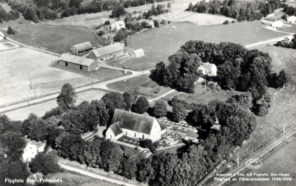 Flygfoto över Frösunda kyrka. I förgrunden ligger kyrkan och kyrkogården, den ljusa bygganden är Frösunda prästgård. T v på andra sidan vägen ligger Prästgårdsarrendatorns bostadshus och ekonomibyggnader.