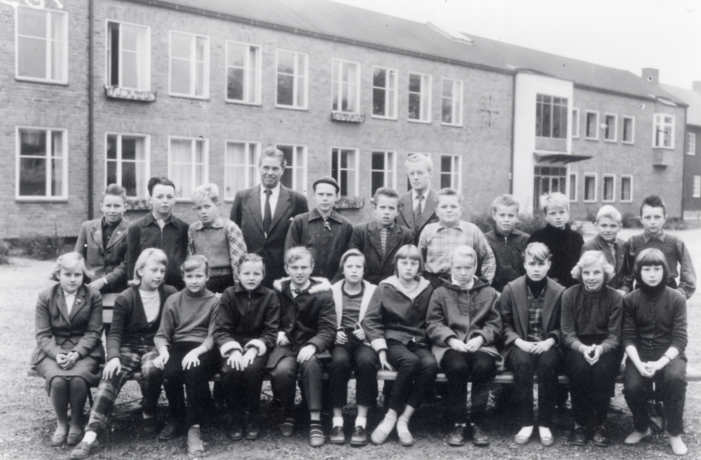 Klass 6 samlad tillsammans med rektor Josef Andersson t v och läraren Åke Fredriksson t h utanför Hjälmsta skola.  Övre raden fr v Lars-Erik Rickberg, Jan-Olov Lund, Åke Brodd, Karl-Ivar Lindblom, Hadar Axh, Glenn Söderberg, Bjarne Karlsson, Olle Svenander, Lennart Tillborg och Lars Jansson. Sittande fr v Noomi Broman, Lillemor Holmberg, Ulla Johansson, ?, Ingrid Rydell, Anita Ek, Ing-Marie Söderman, Birgitta Hofgren, Gunilla Felldin, okänd och Siv Pettersson