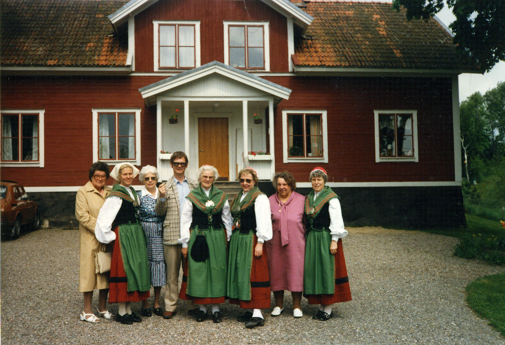 Kyrkoherde Tom Wallgren utanför Angarns församlingshem, omgiven av damer, de flesta klädda i Össeby-dräkten.  Fr v Karin Eriksson, Harriet Edgren, okänd, Tom Wallgren, okänd, Lilly Öhlin Lundby, Karin Jansson Rävsta och Ingegerd ?