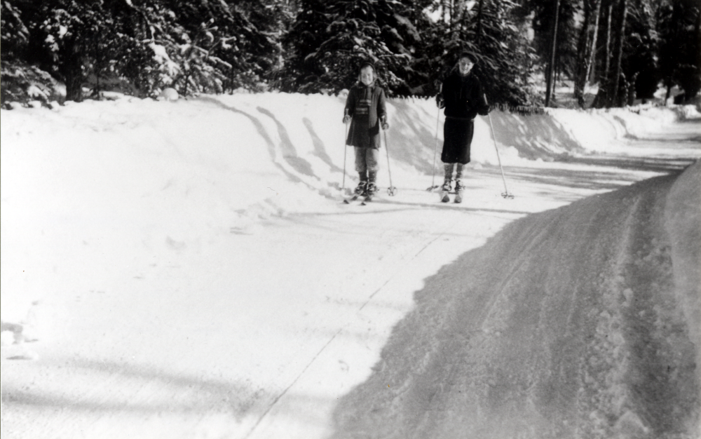 Fotografens systers barn Kajsa och Buster  Glassel på skidtur längs Lingsbergsvägen påsken 1951.  Höga vallar har plogats på vägen, för vintern 1951 var ovanligt snörik med en snödjup på över en meter. Rättelse 2021-07-09: Enligt nya uppgifter är det fotografens systers barn, inte brorsbarn som tidigare angavs.