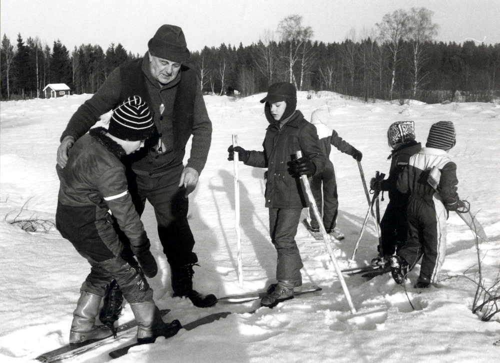 Martin Linder visar hur man lekte förr.  Martin levde 1908-1996.  Tillsammans med några barn har Martin gjort skidor av brädor, laggar från tunnor vid torpet i Grävelsta.  Jfr uttrycket "klämma lagg" vid skidåkning!  Enligt Martin kallades det att åka skarskidor i Vallentuna.  Här hjälper Martin fr v Calle Rahmquist, övriga barn fr v ? Ek, okänd, Katarina Karlsson och Lars Eriksson?