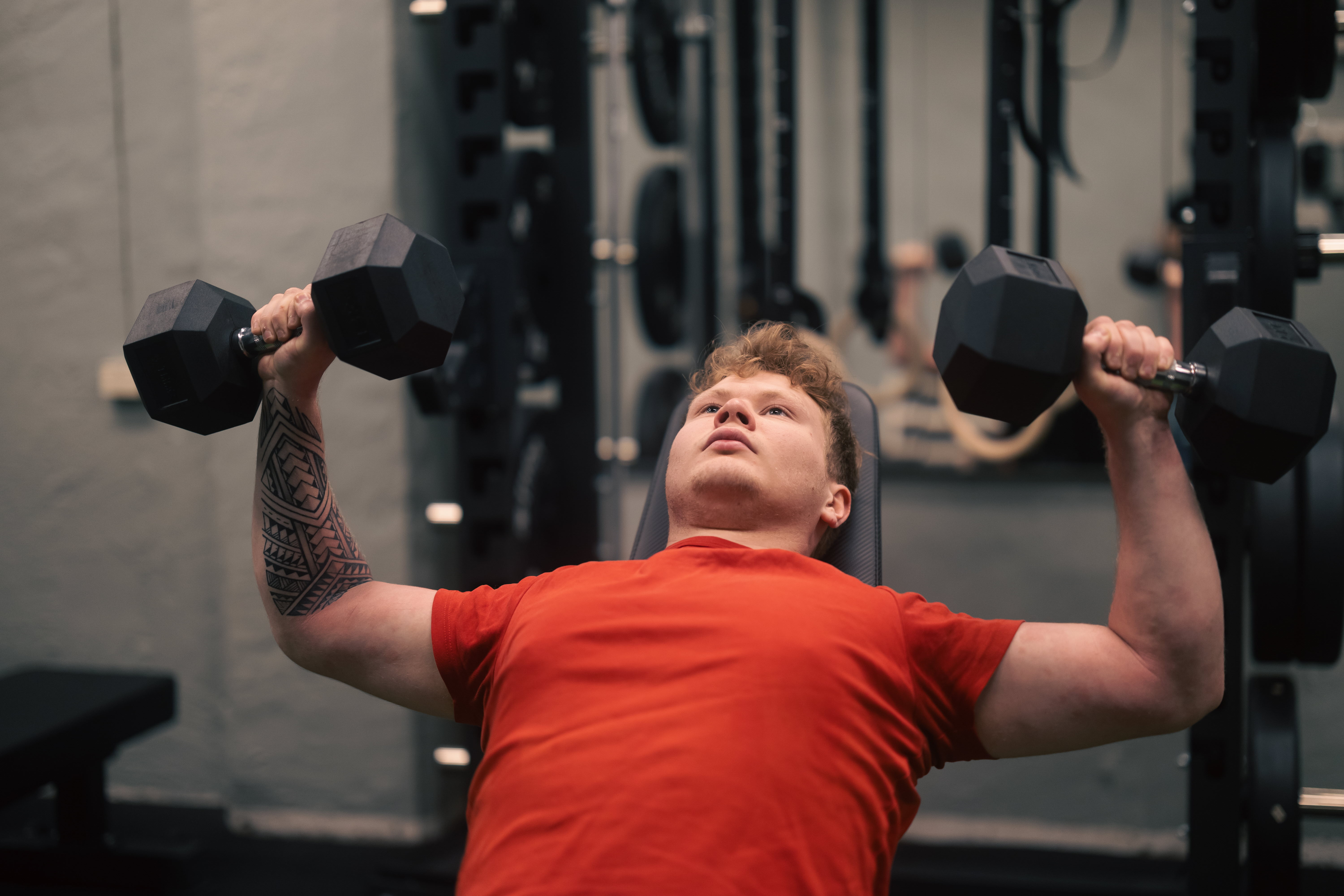 Elev halvsitter i gymstol med en hantel i vardera hand.