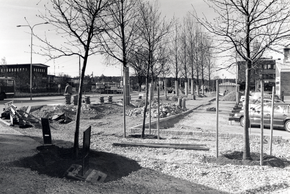 Banvägen i Vallentuna centrum byggs om våren 2000.  Utsikt mot söder.  Arbetena påbörjades hösten 1999, med uppehåll under vintern.  Här syns syns den nya gång- och cykelbanan där busshållplatsen flyttas tillbaka i september.  Tillfälligt har bussarna stannat utanför Tunahuset.  T h skymtar gaveln på Tunahuset och Torghuset.  T v Vallentuna gymnasium på andra sidan järnvägen