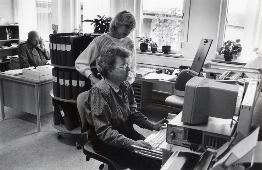 Vallentuna gymnasium.  Skolans expedition.  Vid telefonen t v sitter arkitekt Cederwall, sittande vid skrivbordet med datorn Solveig Lång och stående Anita Ferde