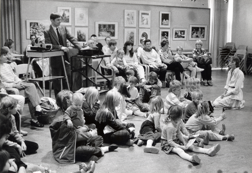 Under tiden 2-31 oktober 1985 pågick i Tärningen utställningar, program, sång, dans, musik och föreläsningar m m under tema På Bellmans tid Arrangörer var föreningar i Vallentuna i samarbete med Kulturnämnden. Idé och utformning: Eva Rahmqvist och Helen Ericsson Här pågår 1700-talet får liv Anne Banér levandegör en målning inför barn och vuxna i Vallentunasalen. I programmet ingick projecering av diabilder föreställande en tavla, när sedan draperierna drogs ifrån fanns tavlans personer levande på scenen. Vid projektorn står Gunnar Hillbo Anne Banér sitter på golvet framför barnen.