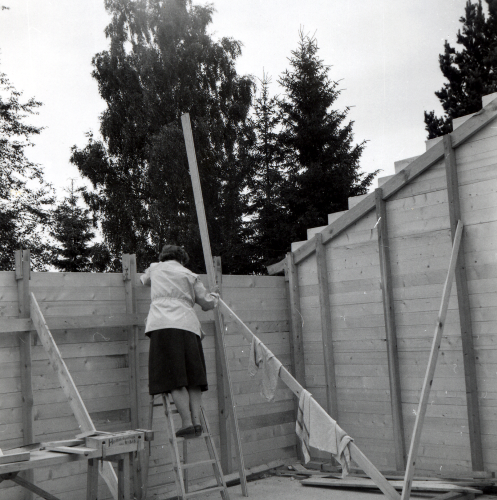 Norrängsvägen 5 - väggarna är resta.  Ulla Gustafson står på en stege.  "Färdigt för takstolarna".