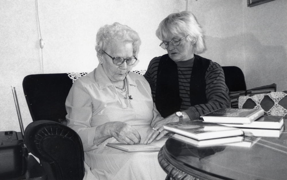 Signe Bäckström på Väsbygården får böcker av hemtjänstens Kajsa Kirnär via bibliotekets Boken kommer-verksamhet – böcker direkt hem till den som inte själv kan besöka biblioteket